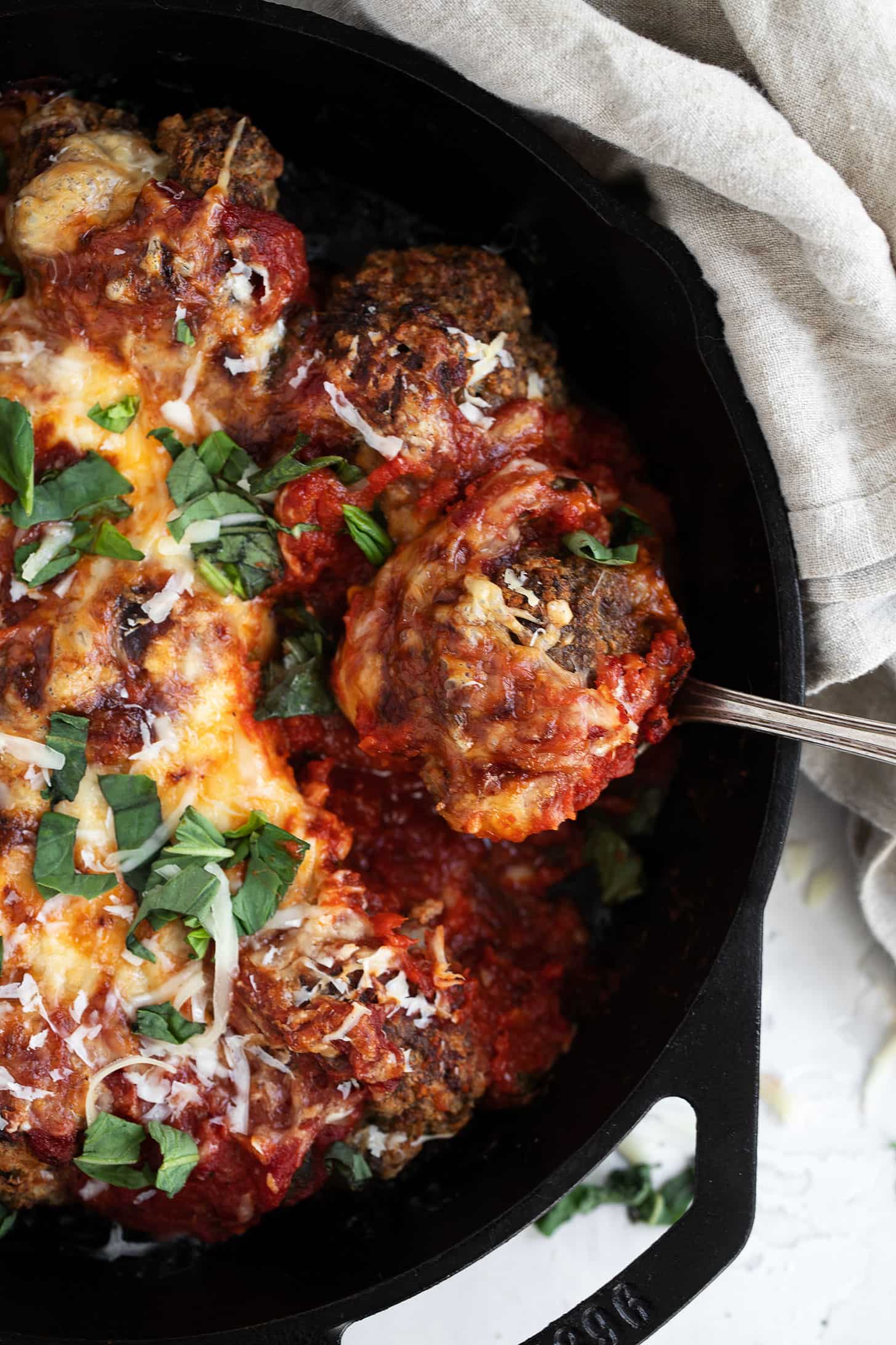 cheesy baked meatballs and tomato sauce in skillet with spoon