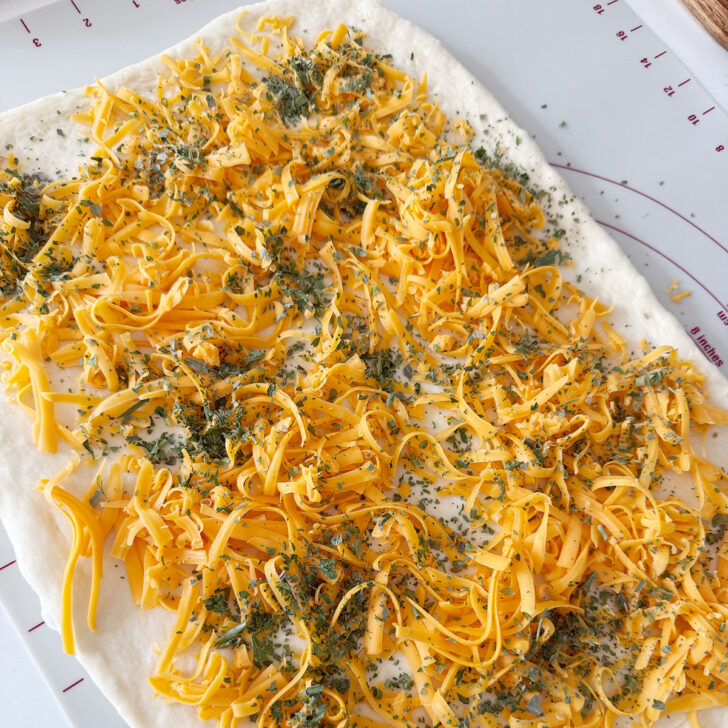 Dough rectangle scattered with cheddar cheese and herbs.