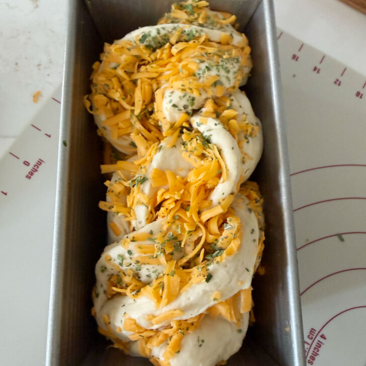 Shaped cheese bread placed into a loaf pan.