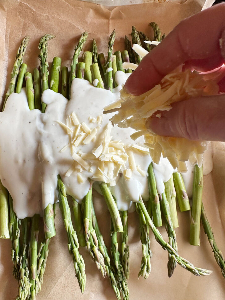 white sauce poured over asparagus on baking sheet