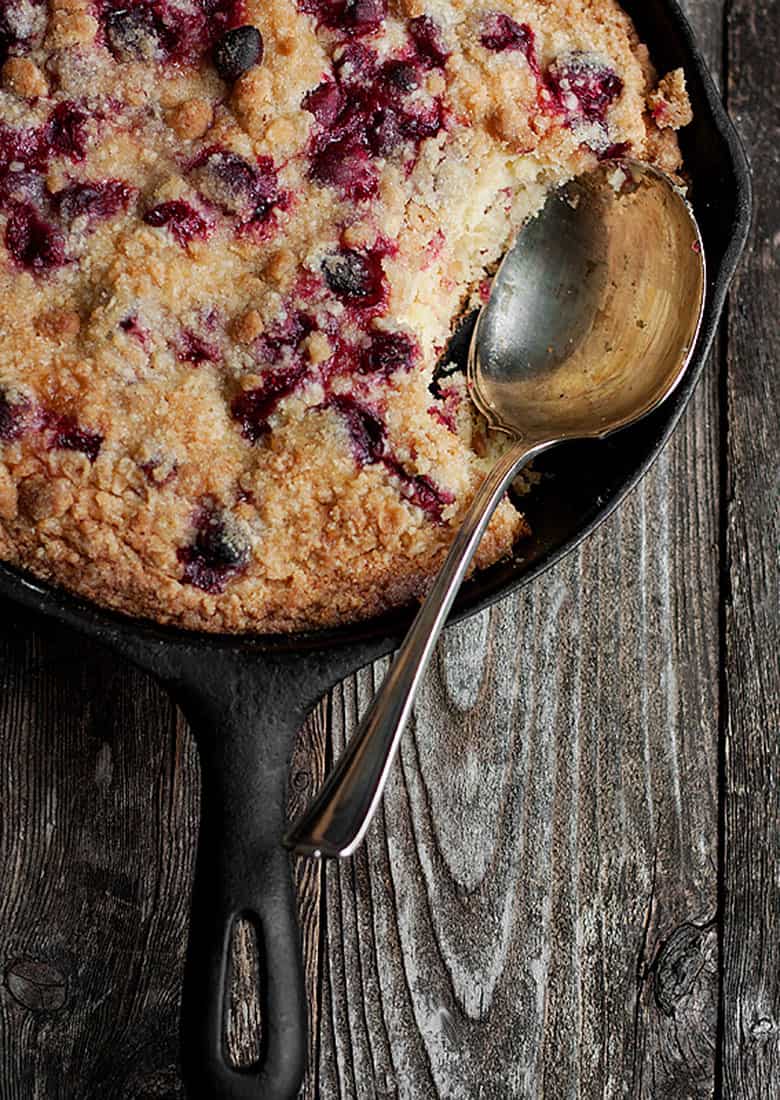 cranberry buckle cake in cast iron skillet with spoon