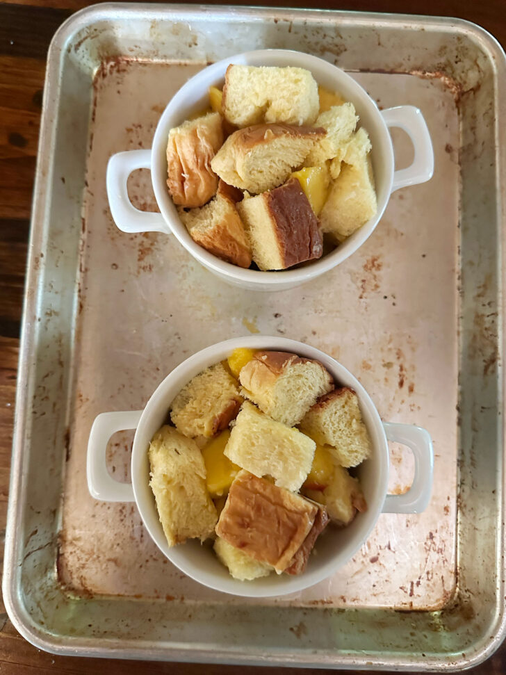 bread cubes and peaches in ramekins on a baking sheet