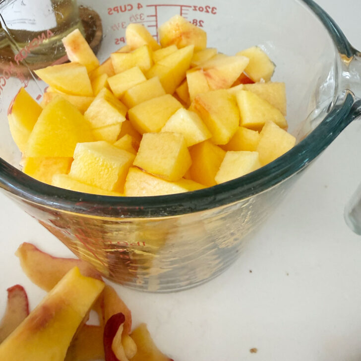 Peeled and pitted peaches cut into chunks in a large measuring cup.