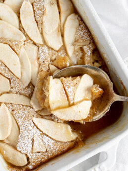 apple pudding cake in baking dish being spooned out