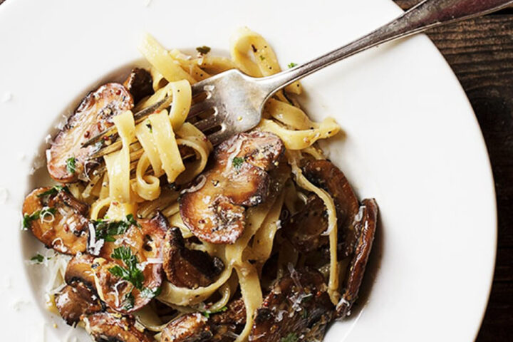 creamy mustard pasta with mushrooms in white bowl with fork