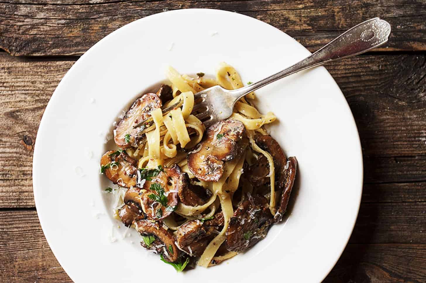 creamy mustard pasta with mushrooms in white bowl with fork