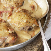 chicken thighs with apple and bacon in pan with spoon