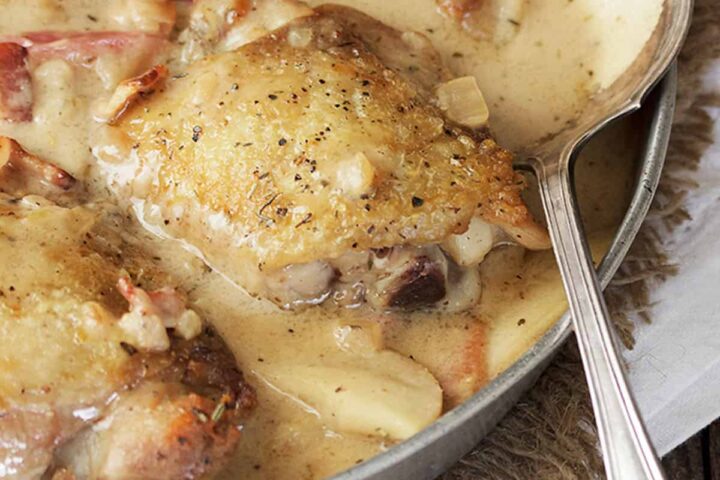 chicken thighs with apple and bacon in pan with spoon