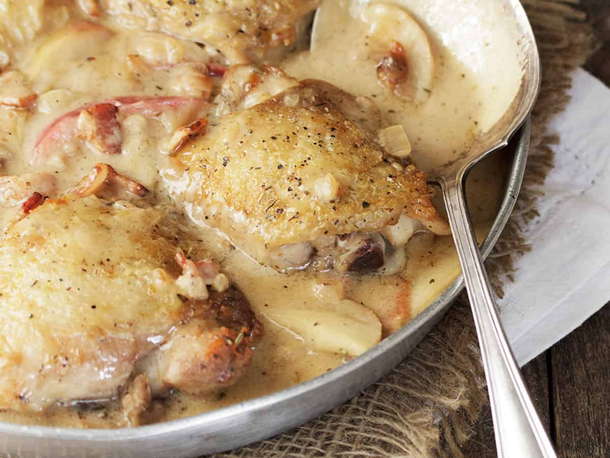 chicken thighs with apple and bacon in pan with spoon