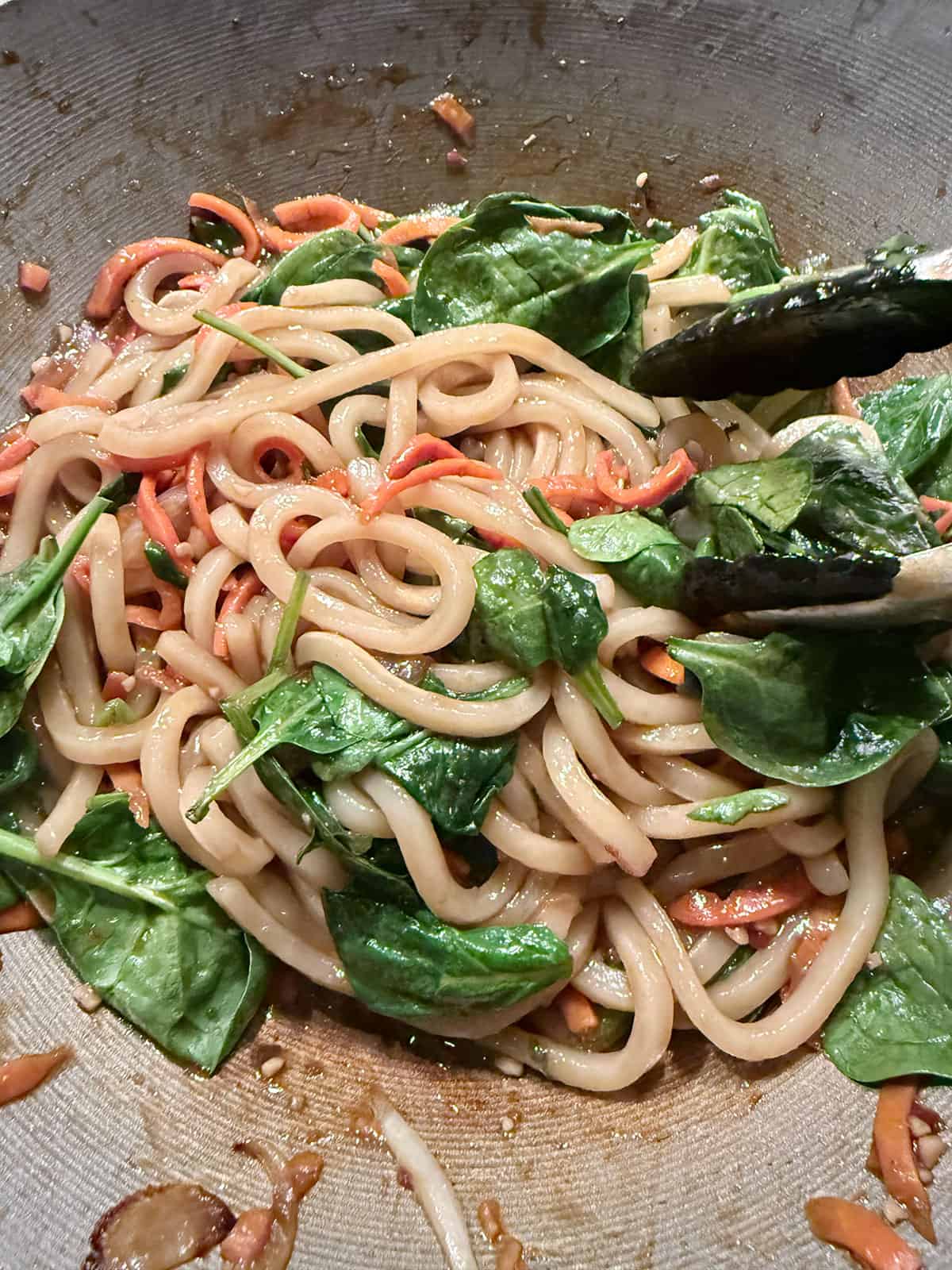 Baby spinach added to the wok with the udon noodles, spicy sauce and vegetables.