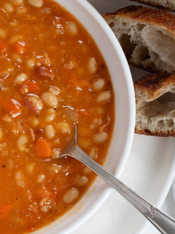 bean with bacon soup in bowl with bread slices on the side