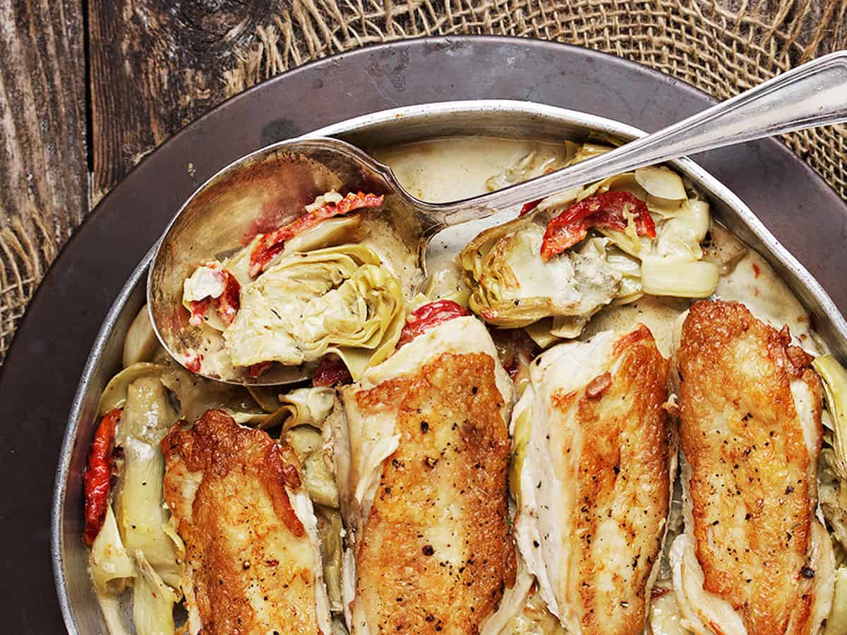 chicken with artichokes and sun dried tomatoes in pan with spoo
