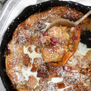 Rhubarb bread pudding in a cast iron skillet with a spoon.