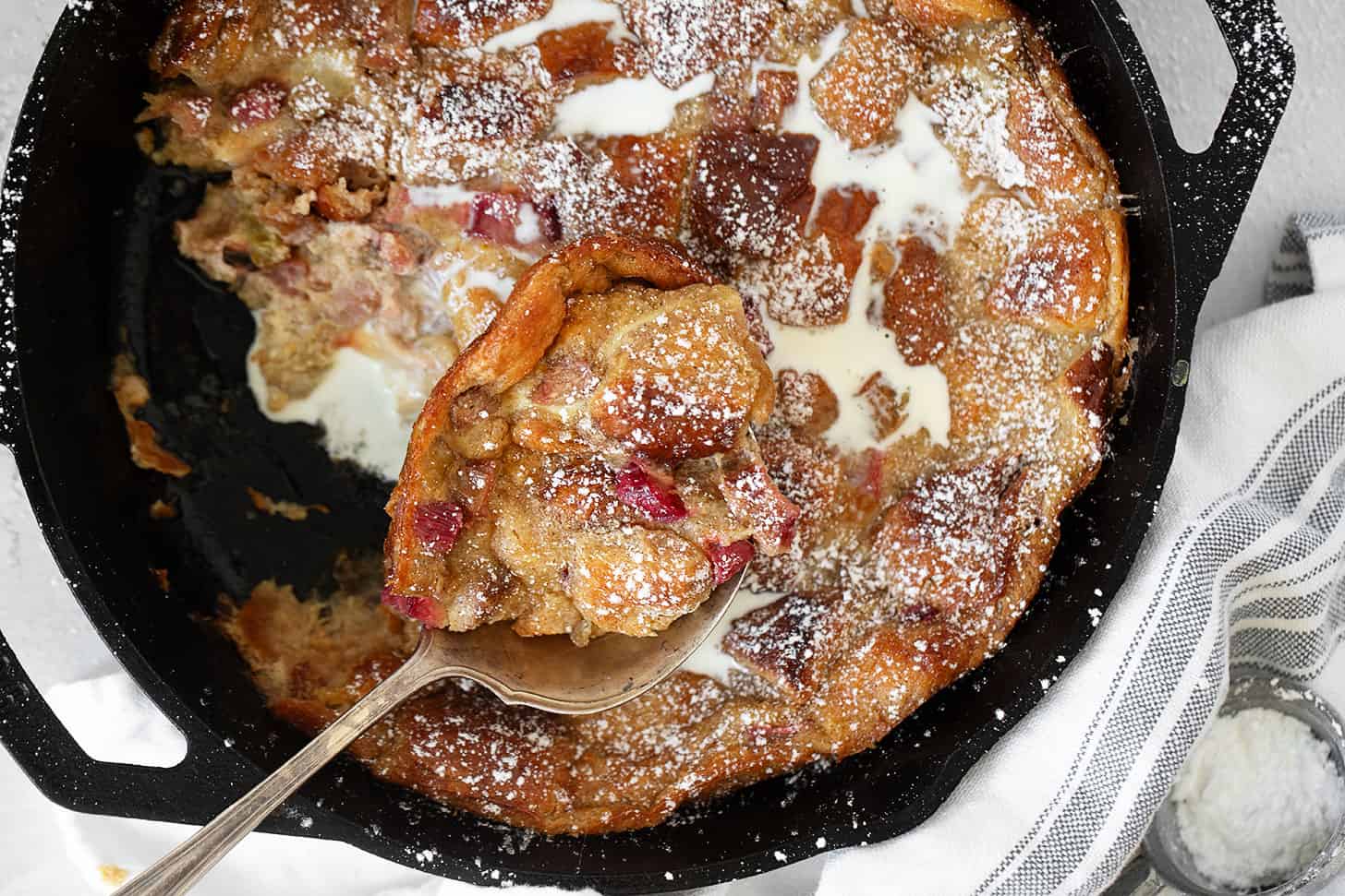 Rhubarb bread pudding in a cast iron skillet with a spoon.