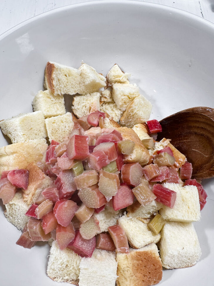 Adding cooked rhubarb to a bowl with cubed bread.