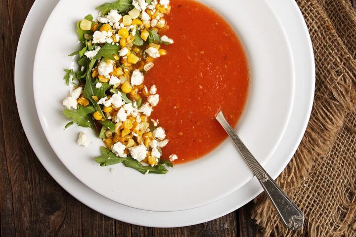 tomato soup in white bowl, garnished with corn and feta