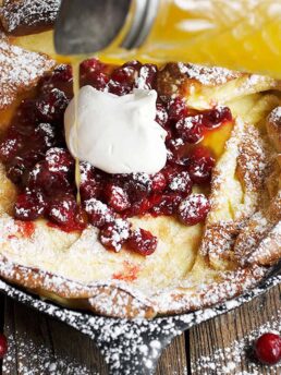 Dutch baby with cranberries on top pouring orange syrup
