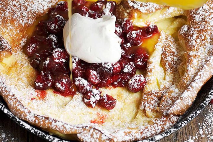 Dutch baby with cranberries on top pouring orange syrup