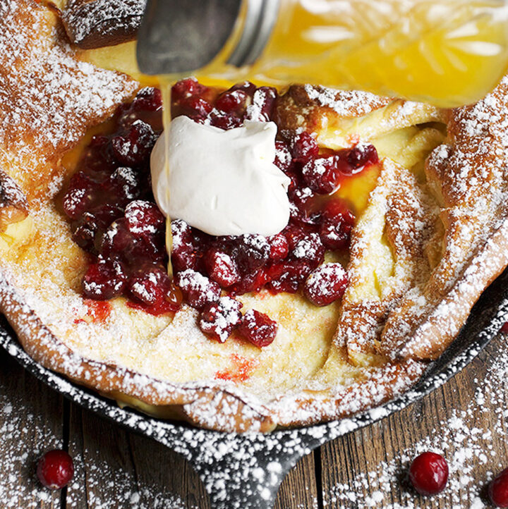 Dutch baby with cranberries on top pouring orange syrup