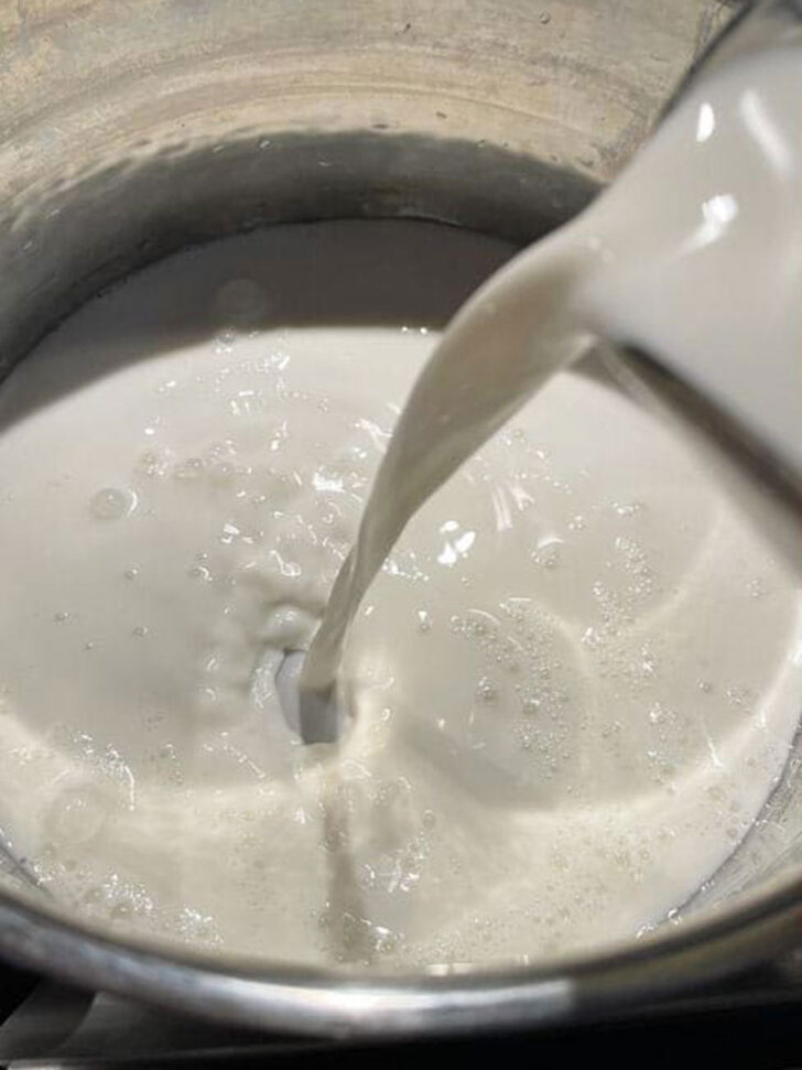 Adding milk to the cooking pot.