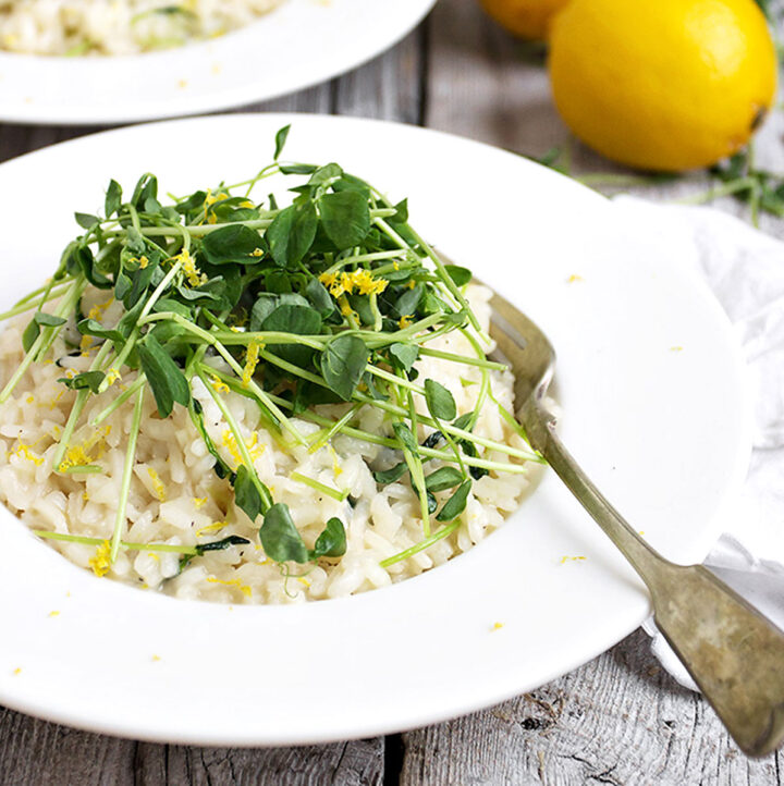 lemon risotto with peach shoots on top in white bowl with fork