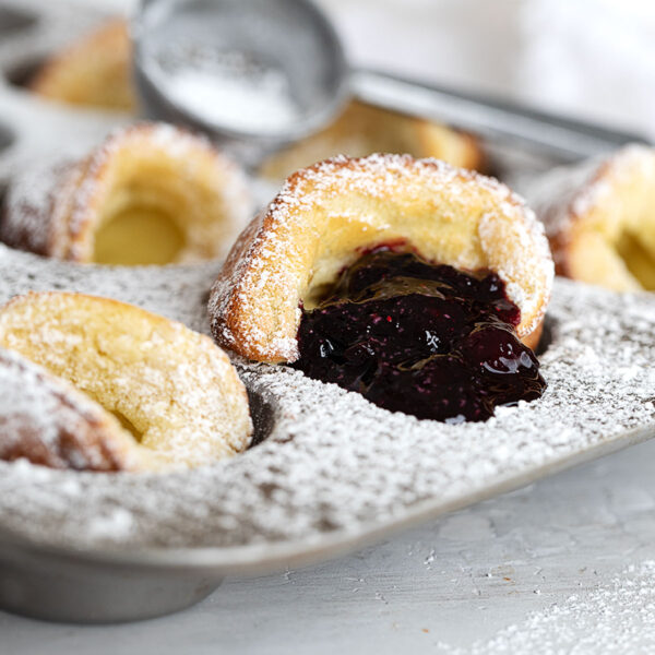 mini Dutch babies in muffin tin with blueberry sauce