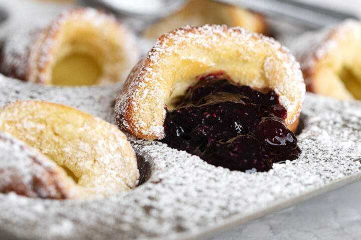 mini Dutch babies in muffin tin with blueberry sauce