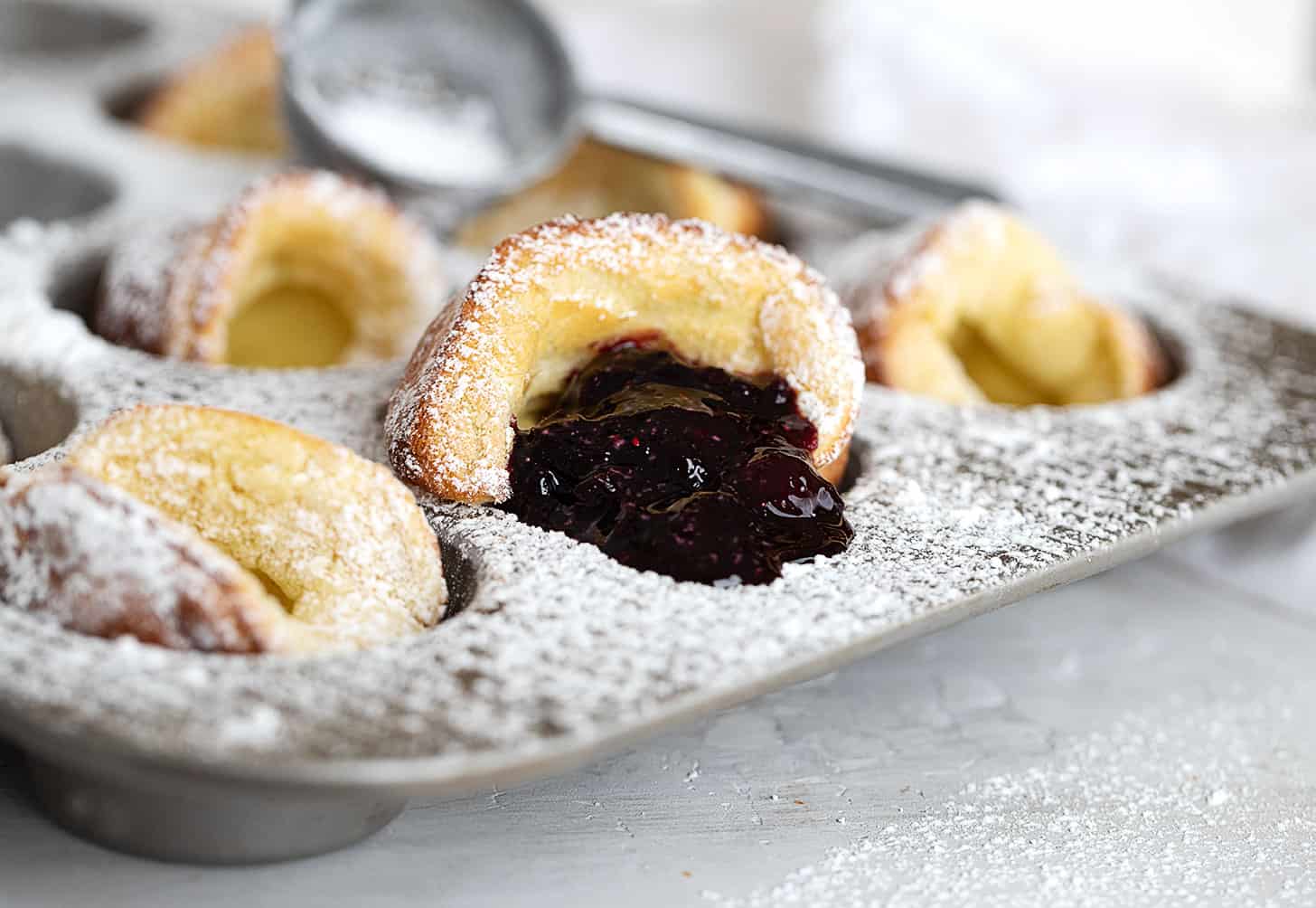 mini Dutch babies in muffin tin with blueberry sauce