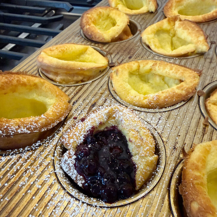 Mini Dutch baby pancakes in the muffin tin, with one filled with blueberry sauce.