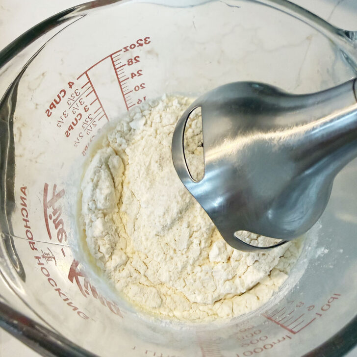 Dutch baby batter ingredients in a large measuring cup with an immersion blender.