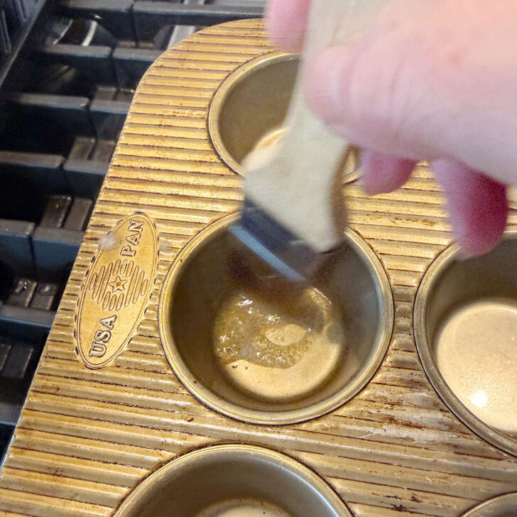 Brushing melted butter into the muffin cups.