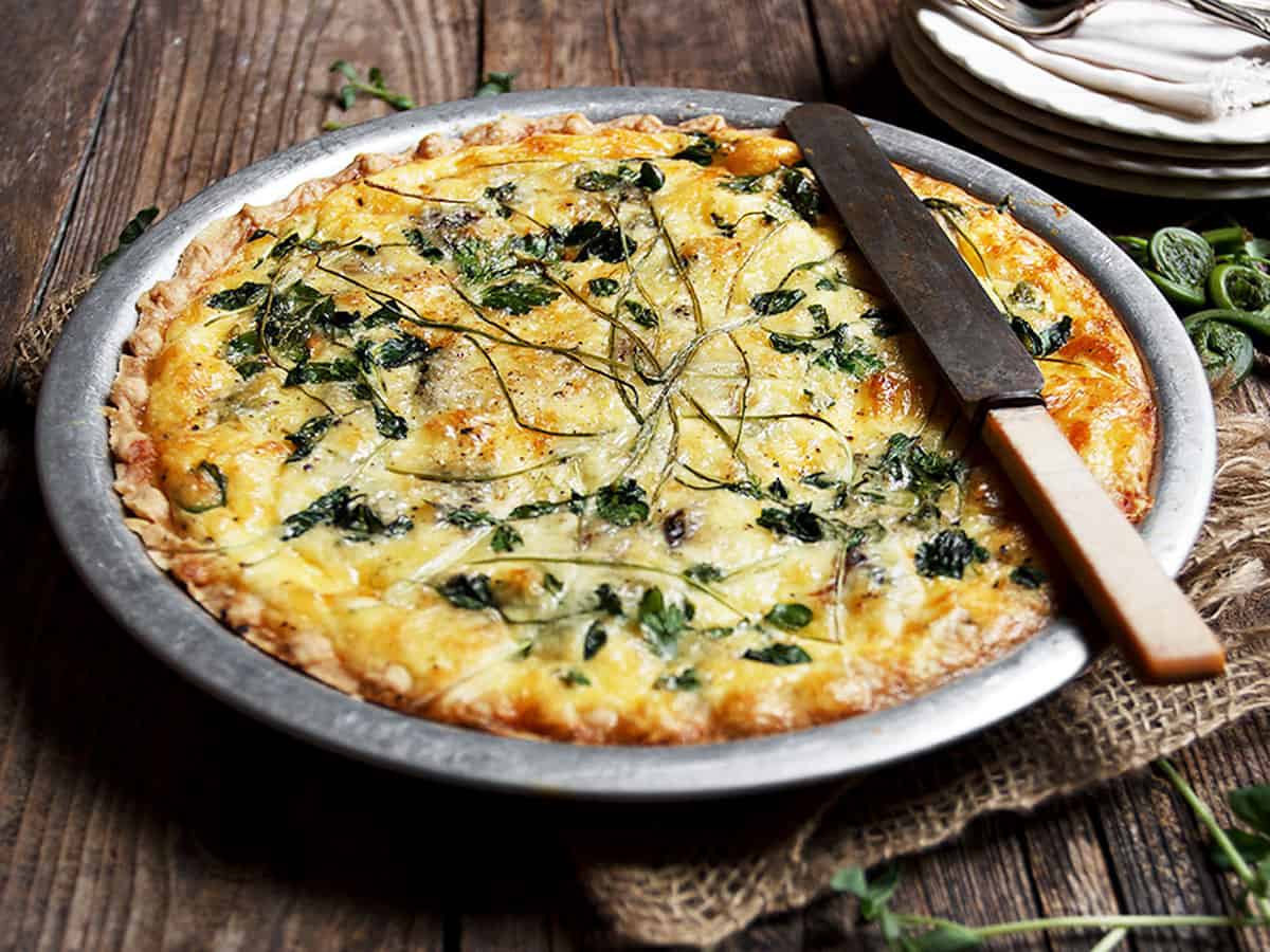 fiddlehead quiche in pie plate with knife