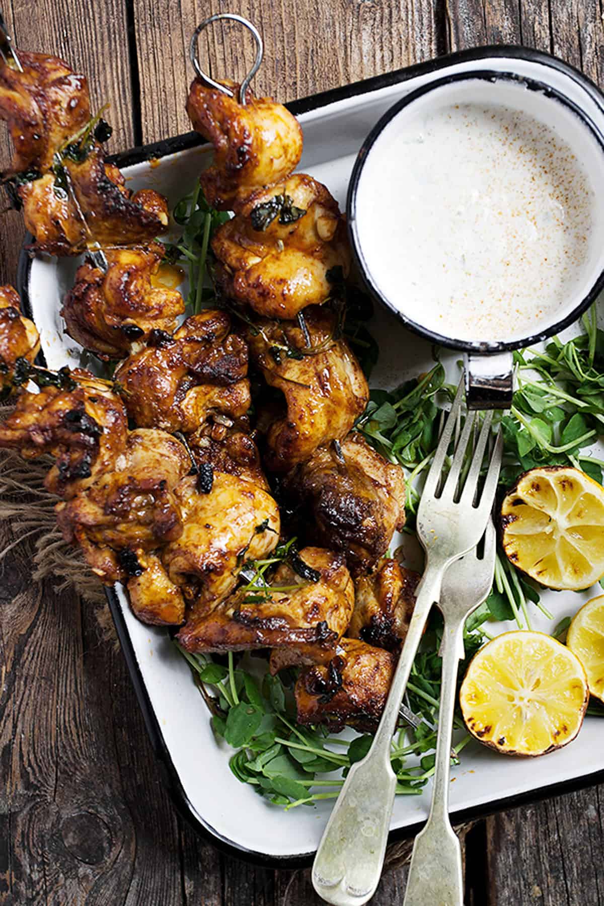 Portuguese chicken skewers on platter with lemons