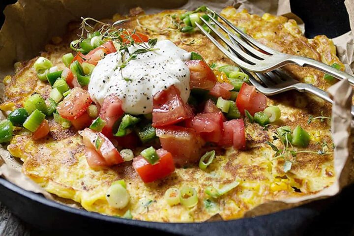 savoury corn pancake in skillet with jalapenos and tomatoes