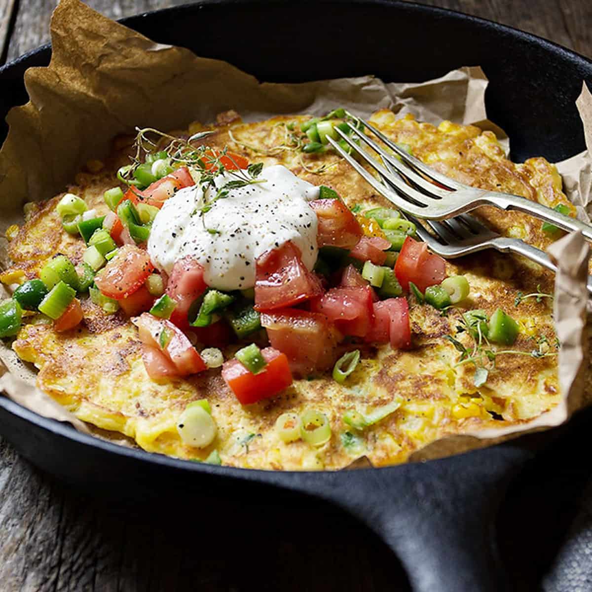 savoury corn pancake in skillet with jalapenos and tomatoes