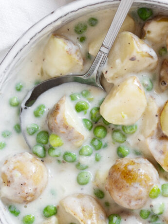 Creamed peas and potatoes in serving dish with spoon.