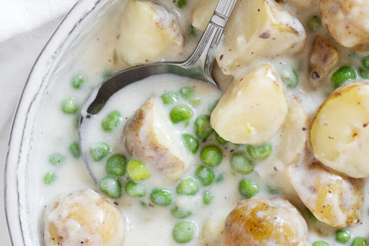 Creamed peas and potatoes in serving dish with spoon.