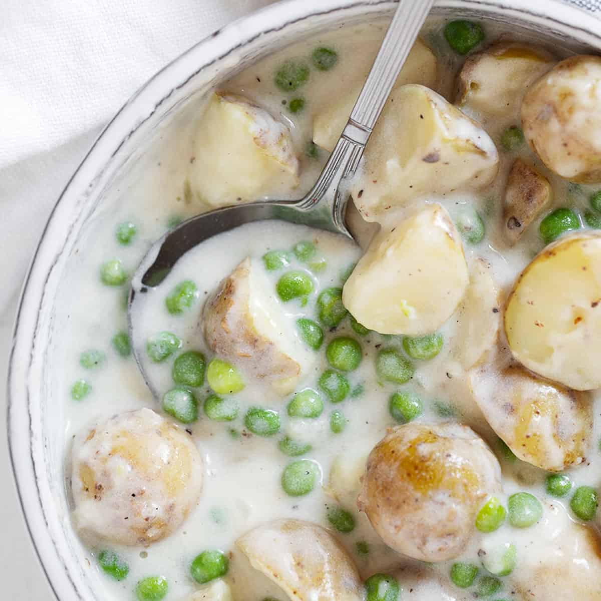Creamed peas and potatoes in serving dish with spoon.