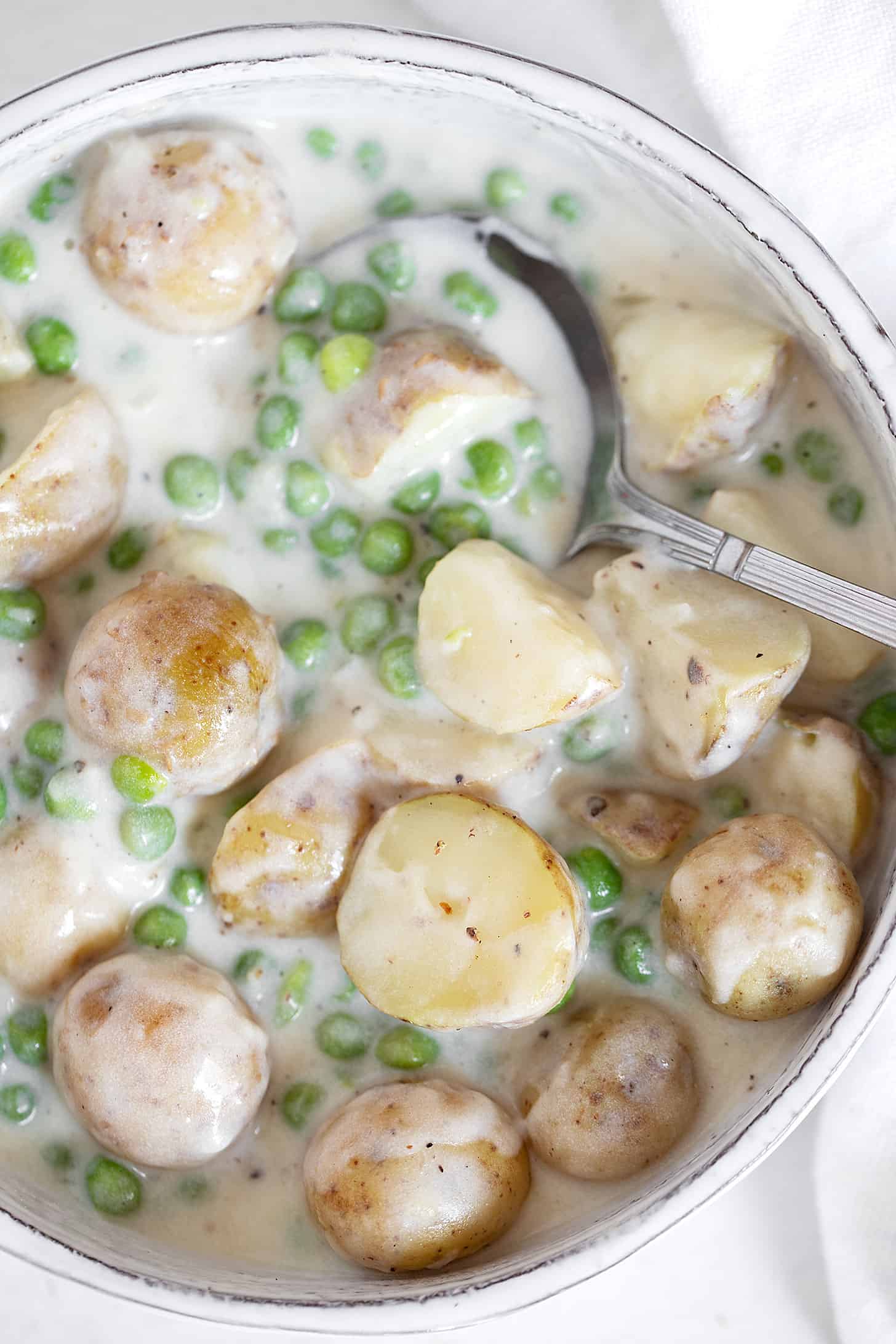 Creamed peas and potatoes in serving dish with spoon.