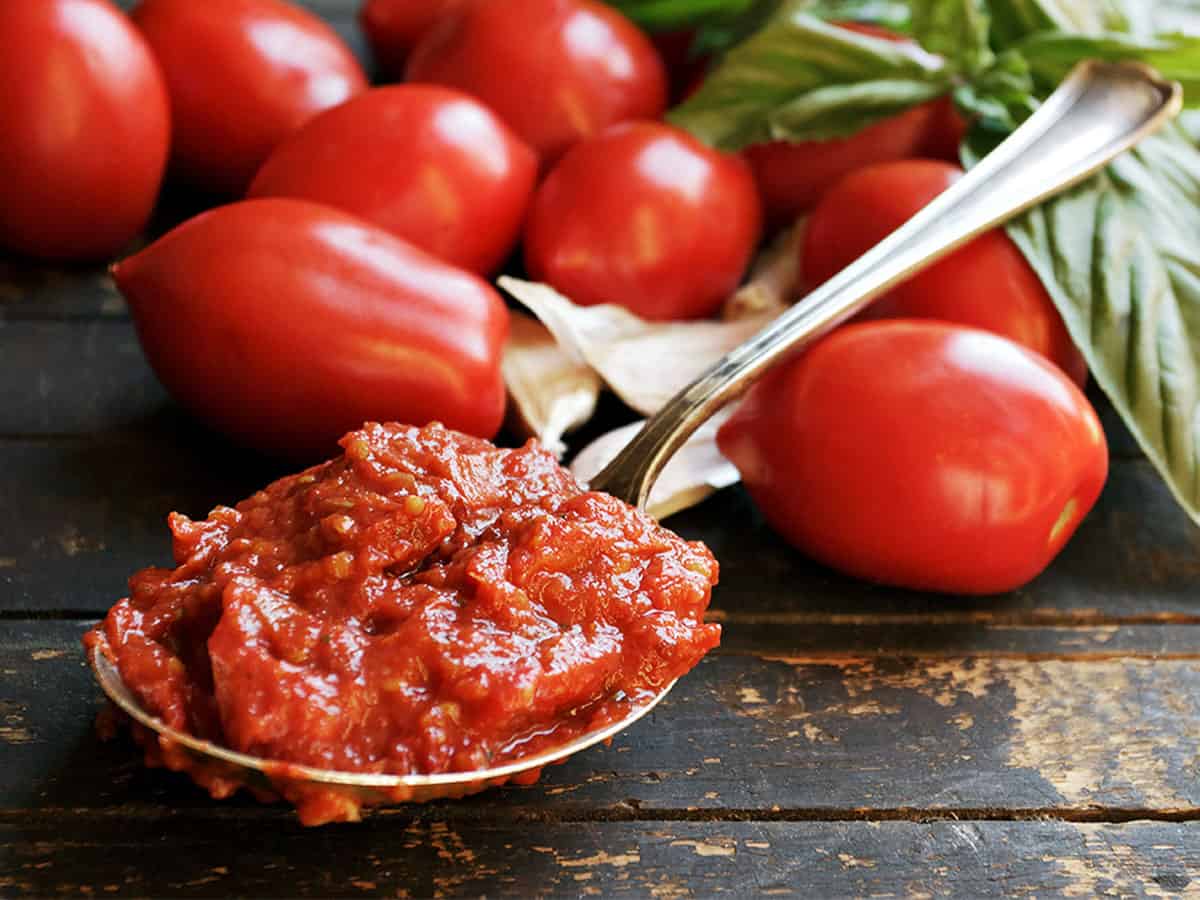 homemade marinara sauce on spoon with tomatoes, basil and garlic