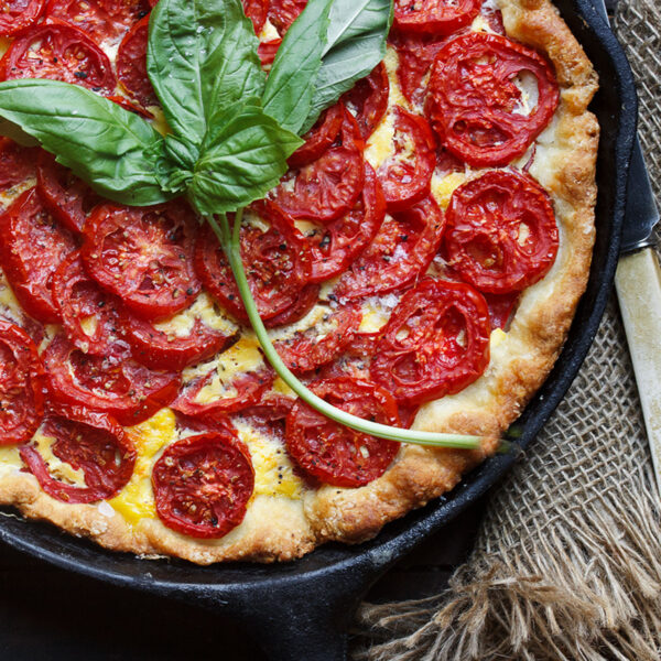tomato cheese pie is skillet with basil leaves