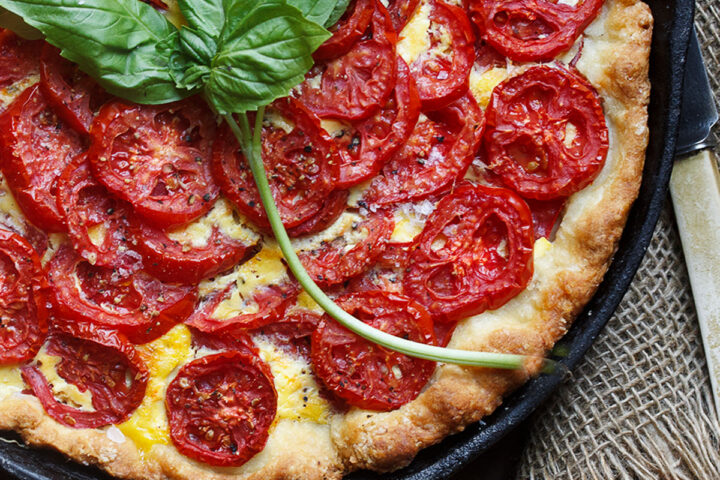 tomato cheese pie is skillet with basil leaves