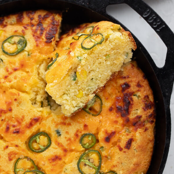 Cast-iron skillet jalapeño cornbread in the skillet with a slice cut out.
