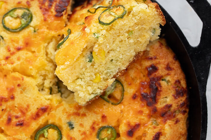 Cast-iron skillet jalapeño cornbread in the skillet with a slice cut out.