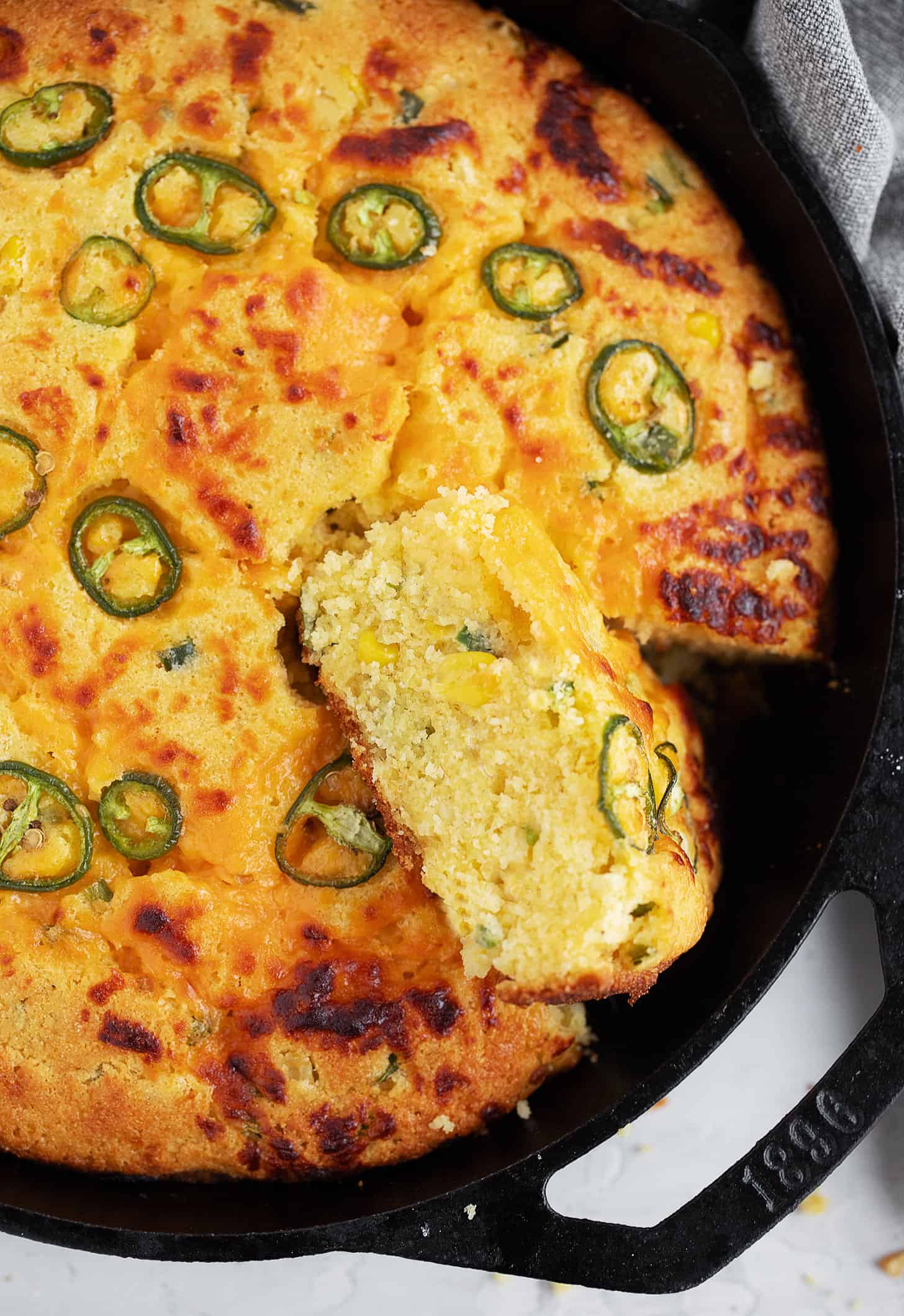 Cast-iron skillet jalapeño cornbread in the skillet with a slice cut out.