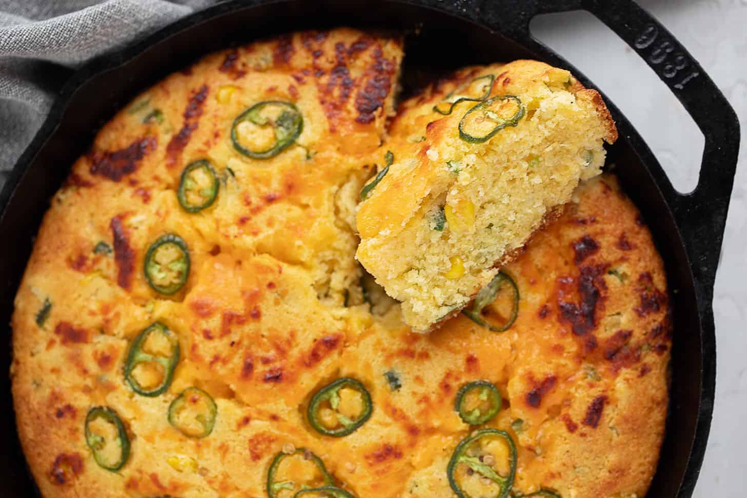 Cast-iron skillet jalapeño cornbread in the skillet with a slice cut out.