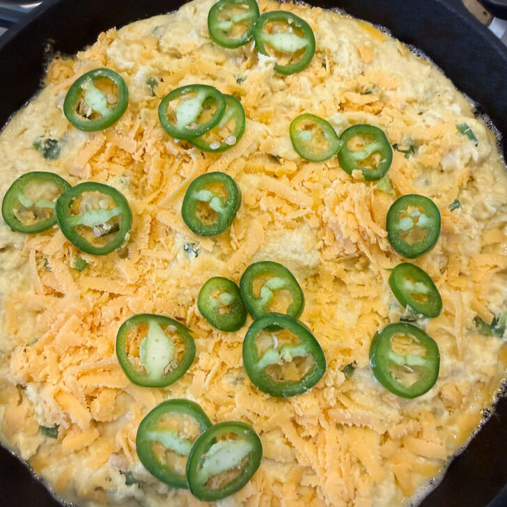 Cornmeal batter added to the hot cast-iron skillet and topped with shredded cheddar cheese and jalapeño slices.