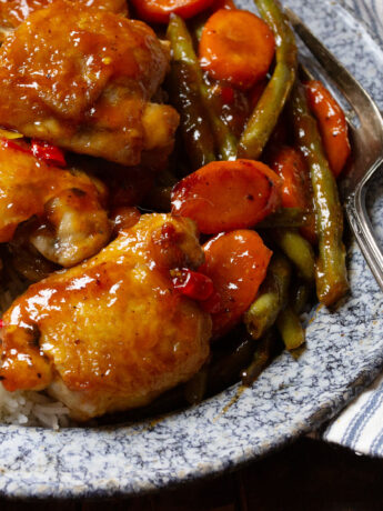 sweet and sour chicken thighs on plate with rice and vegetables