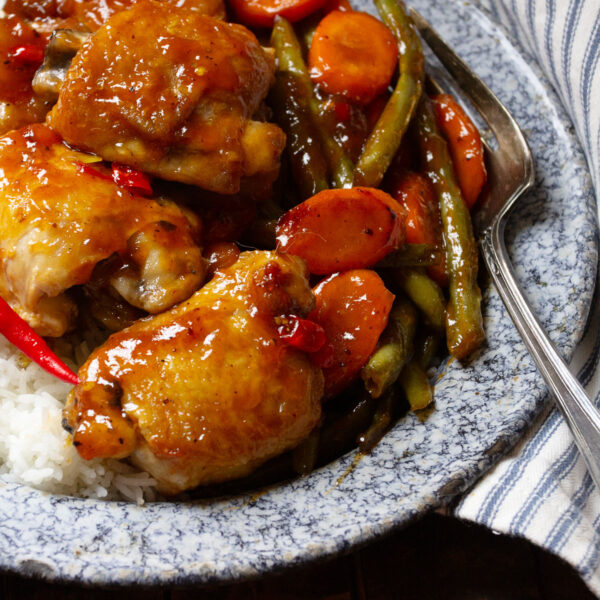 sweet and sour chicken thighs on plate with rice and vegetables