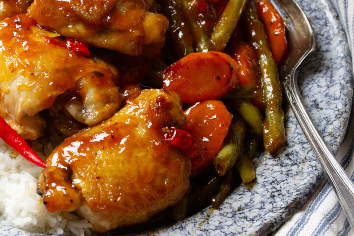 sweet and sour chicken thighs on plate with rice and vegetables